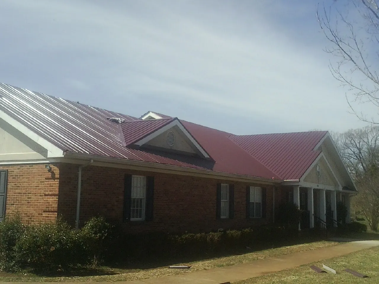 Red metal roof with gabled entries on a long brick building, from a Hail Damage Roof Repair job in Havertown