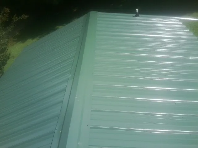 New green metal panels meeting at the ridge of a roof — Flat Roof Repair work by our crew in Havertown