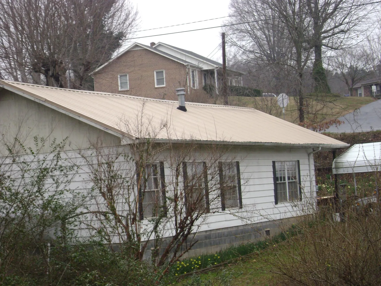 Tan metal roof on a white sided house set into a hillside — Commercial Roofing by Roofing Brothers in Havertown